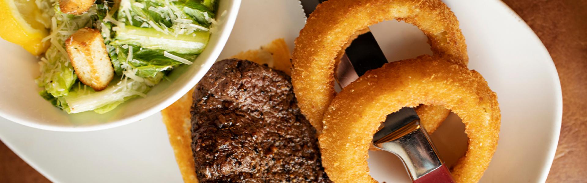 A plate a full rack of baby back ribs glazed in bourbon BBQ sauce served with onion rings  & bowl of caesar salad 
