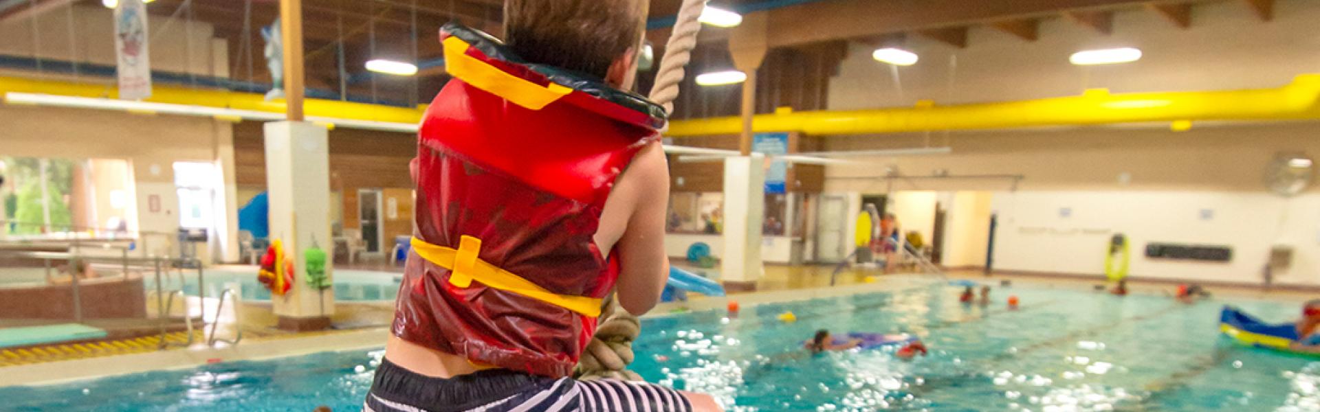 Boy swinging on the Tarzan swing into the pool