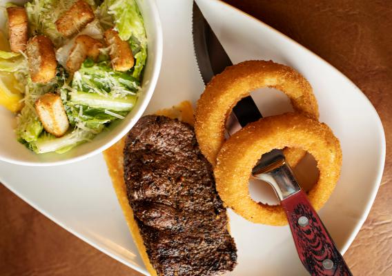 A plate a full rack of baby back ribs glazed in bourbon BBQ sauce served with onion rings  & bowl of caesar salad 